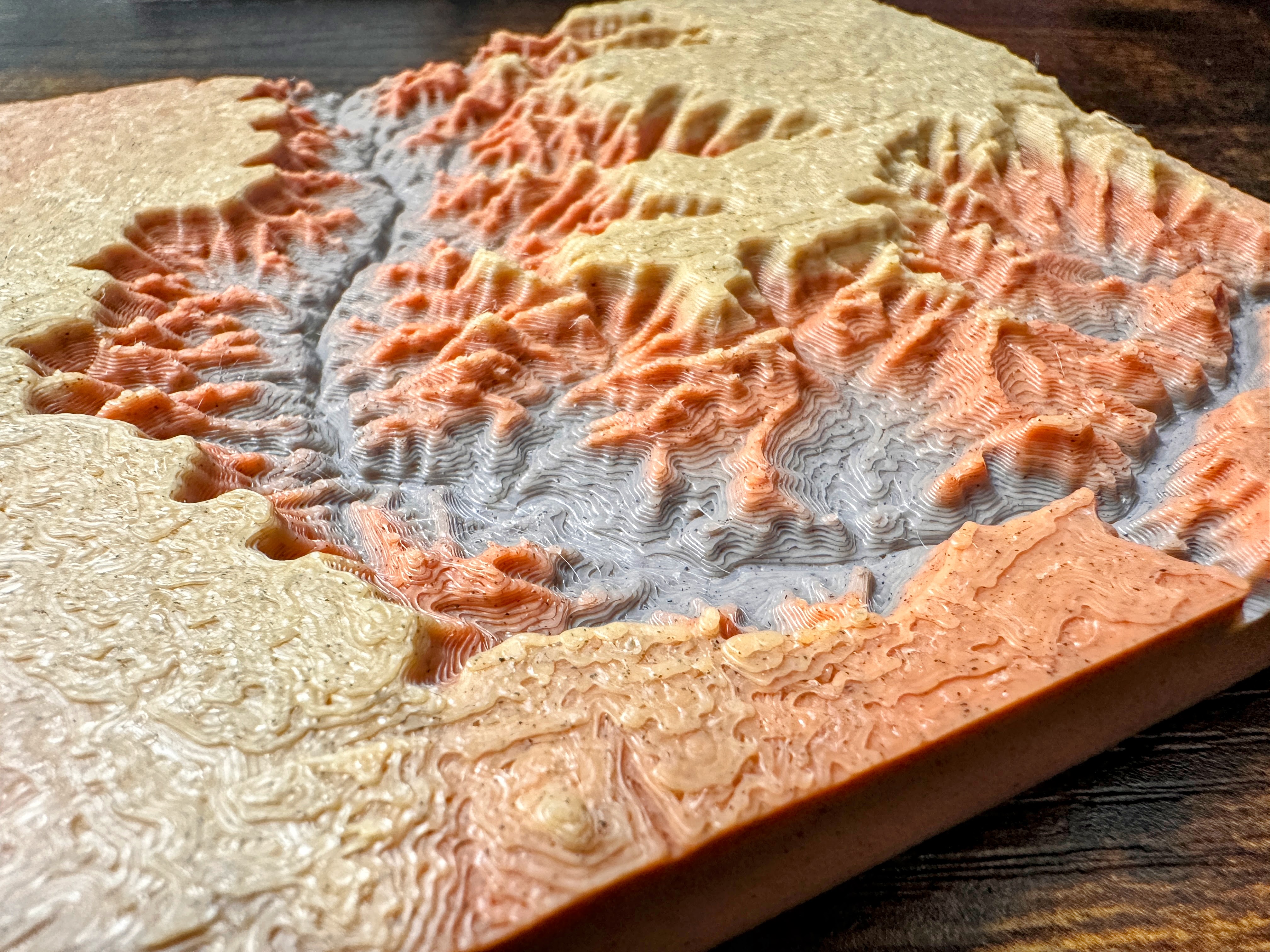 Canyon Ministries Grand Canyon 3D Model A close-up of a colorful 3D-printed topographic map featuring raised, layered terrain in orange, beige, and gray valleys and ridges.