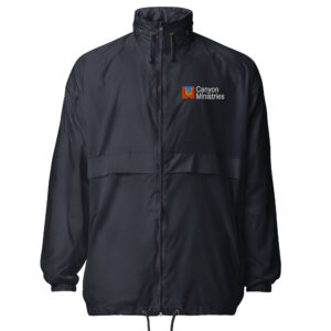 The Windbreaker Rain Jacket is a black zip-up with a high collar, elastic cuffs, and bottom drawstrings. The left chest displays the Canyon Ministries logo featuring an orange, green, and white graphic with bold white text.