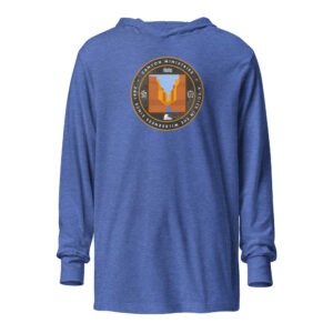 The blue Hooded Long-Sleeve Guide Shirt displays a circular logo depicting a canyon and river, encircled by the phrases “Canyon Ministries” and “The God of the Wilderness Awaits.”.